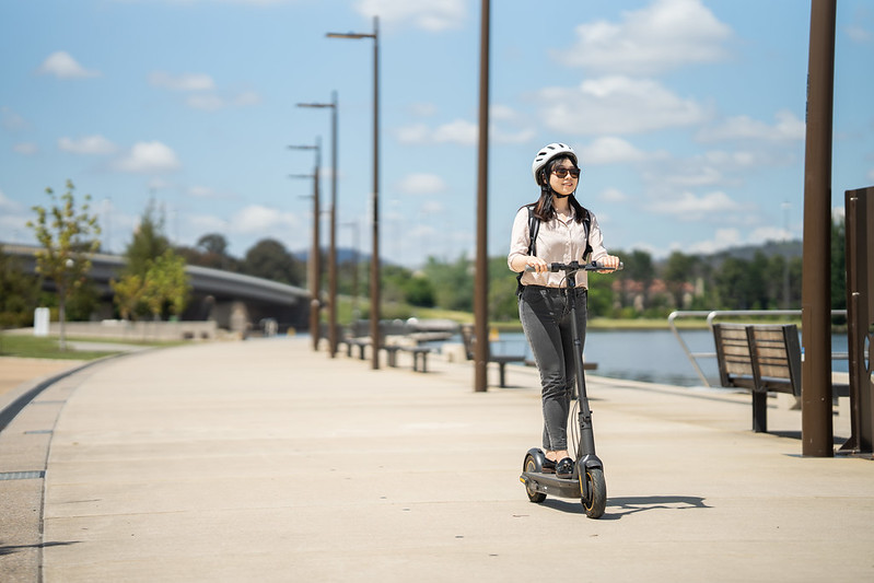 A woman rides an e-scooter by a lake.
