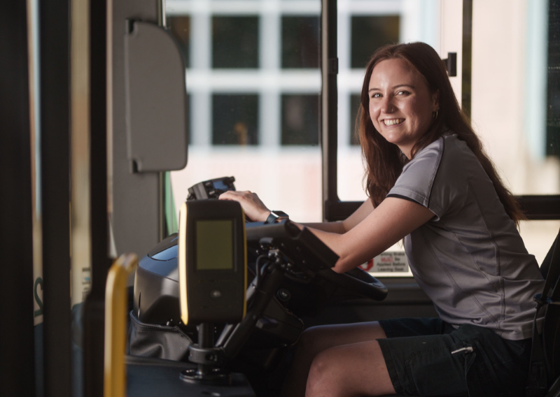Smiling female bus driver in the cabin of the bus.